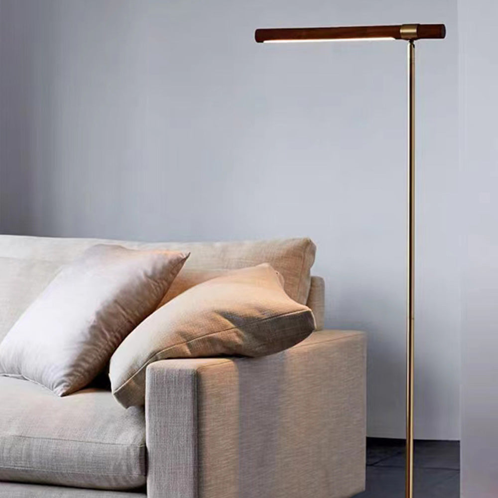 Lampadaire Simon doré avec barre effet bois placé près d’un canapé gris